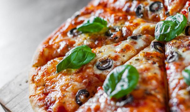 sliced Pizza with Mozzarella cheese, Tomatoes, pepper, olive, Spices and Fresh Basil. Italian pizza. Pizza Margherita or Margarita on wooden table background - Foto, Bild
