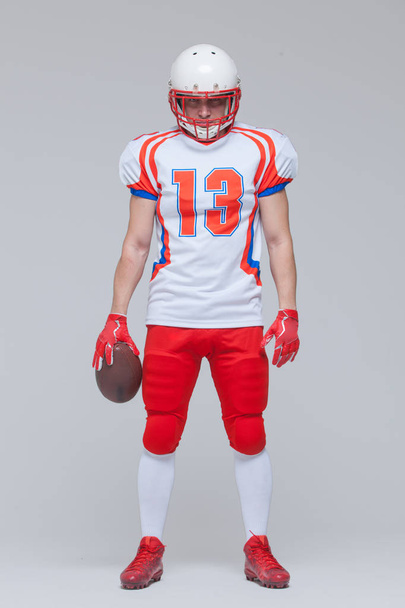 Full length shot of american football sportsman player wearing helmet holding rugby ball isolated on grey background - Foto, Bild
