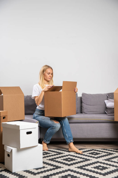 Photo of young blonde with cardboard box sitting on sofa - Photo, Image