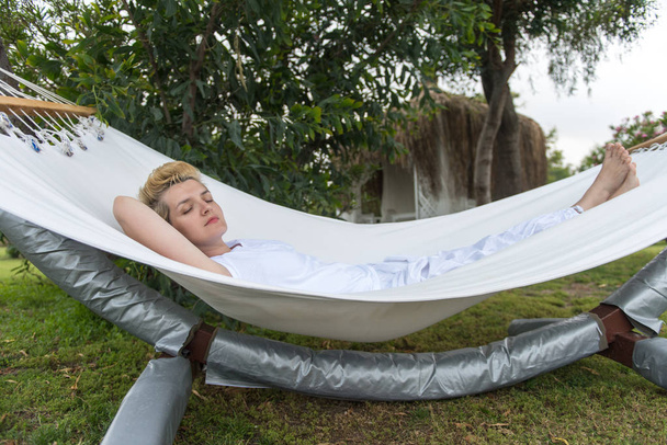 beautiful young woman enjoying free time while resting on white hammock in the backyard - Photo, Image