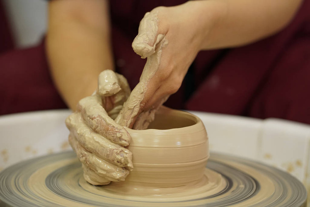 vrouw maakt een kruik met vuil armen op een wiel van Potter uit ruwe natte klei - Foto, afbeelding