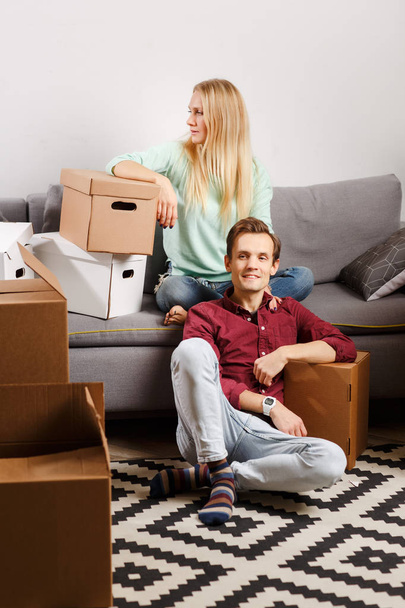 Photo of woman sitting on couch, men sitting on floor among cardboard boxes - Photo, Image