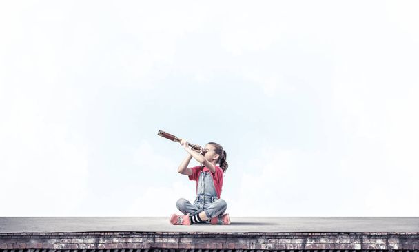 Χαριτωμένο κορίτσι κάθεται στην οροφή του σπιτιού και ψάχνει σε spyglass - Φωτογραφία, εικόνα
