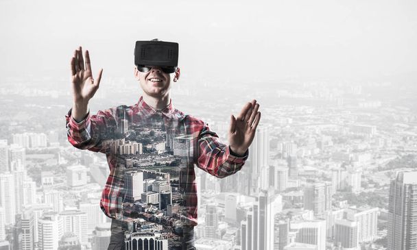 Young man with virtual reality headset or 3d glasses over cityscape background - Фото, зображення