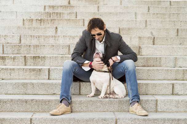 Městská scéna. Muž oblečený v neformálním oblečení sedí na schodech pózuje vedle svého psa - Fotografie, Obrázek