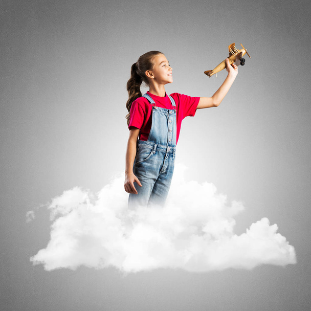 Cute kid girl standing on cloud and playing with airplane toy - Photo, Image