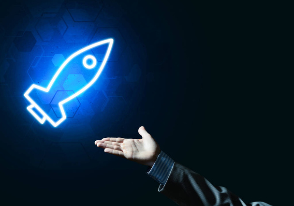 Rocket glowing icon and businessman hand on dark background - Photo, image