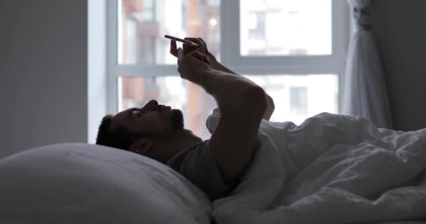 Man lie in his bed with mobile phone - Filmati, video