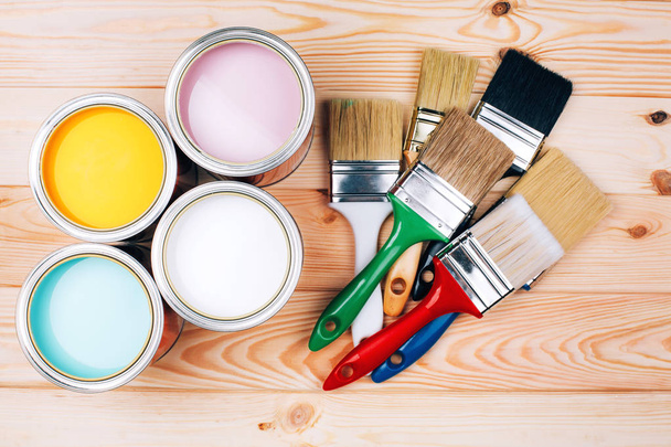 Four open cans of paint with brushes on natural wooden background. - Fotoğraf, Görsel