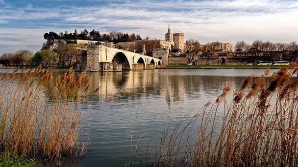 Pohled středověký most přes rákosí na řeky Rhôny z Pont Saint-Benezet_Avignon et Provence napříč řeky Rhôny z břehu řeky Villeneuve-lez-Avignon jako slunce začíná svůj stálý přístup k obzoru. Nad rámec  - Fotografie, Obrázek
