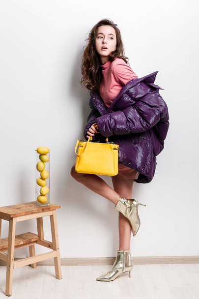 Fashion portrait of young beautiful woman in trendy oversize violet dowm jacket and yellow handbag. Cololrblock. Bright trendy colors. - Foto, afbeelding