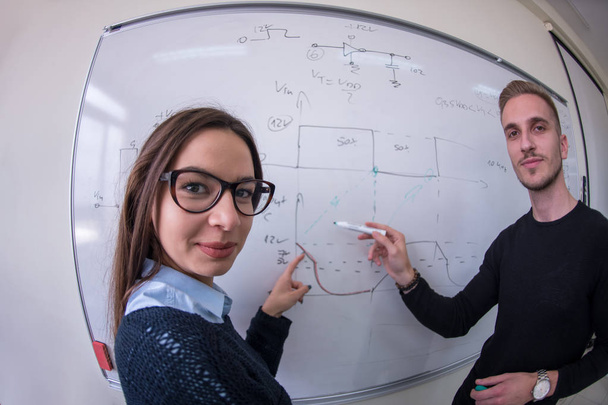 Twee jonge mannelijke en vrouwelijke studenten schrijven op het witte schoolbord tijdens een wiskundeles. - Foto, afbeelding