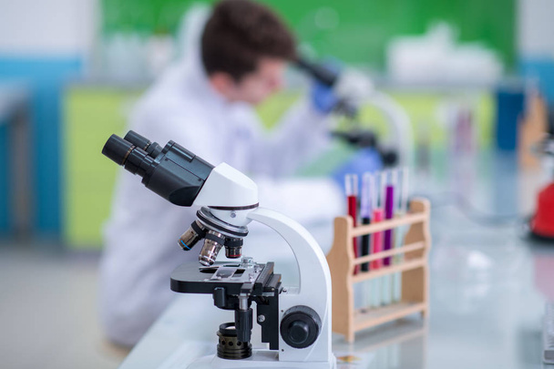 Νεαρός φοιτητής επιστήμονας κοιτάζοντας μέσα από ένα μικροσκόπιο, ενώ κάνει κάποια έρευνα στο εργαστήριο - Φωτογραφία, εικόνα