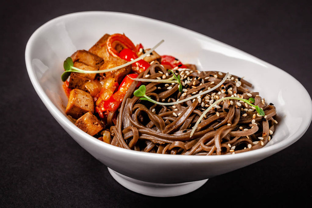 Concept of Asian cuisine. Buckwheat noodles with vegetables and tofu. Carrots, bell peppers, white and black sesame. Japanese or Chinese dish. - Photo, Image