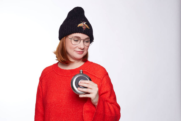 Studio shot of redhead lady with bob hairstyle under knitted hat with strange sick look, being alcohol addict, going to make sip of mortal drink, hiding from family and friends, needs help in rehab. - Photo, Image