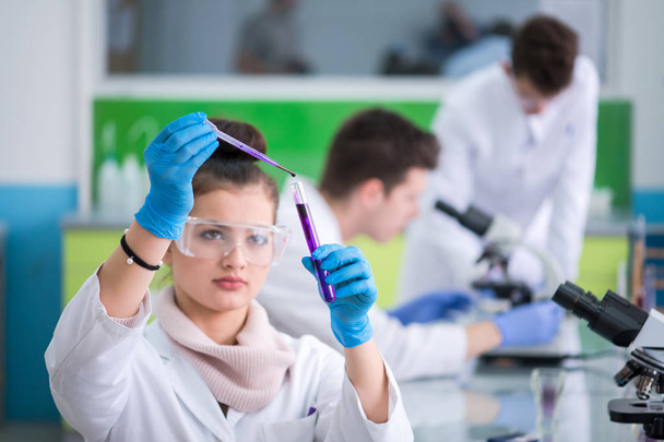 young female student with protective glasses making chemistry experiment in bright laboratory,education and medicine concept - Foto, Bild
