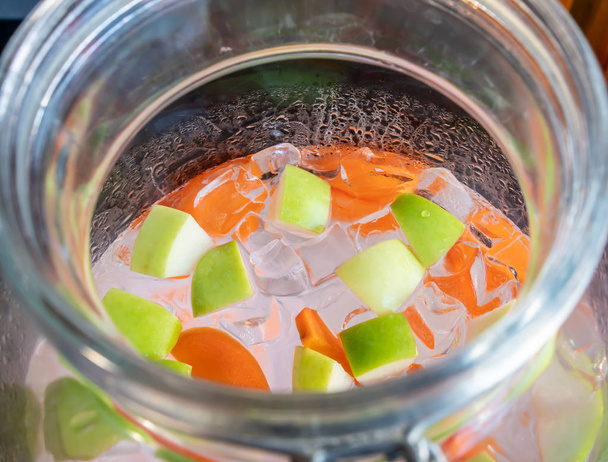 Γκρο πλαν σε πράσινο μήλο, καρότο και πάγο σε γυάλινη φιάλη των φρούτων αρωματισμένο νερό. - Φωτογραφία, εικόνα