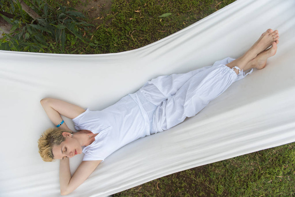 beautiful young woman enjoying free time while resting on white hammock in the backyard - Фото, зображення