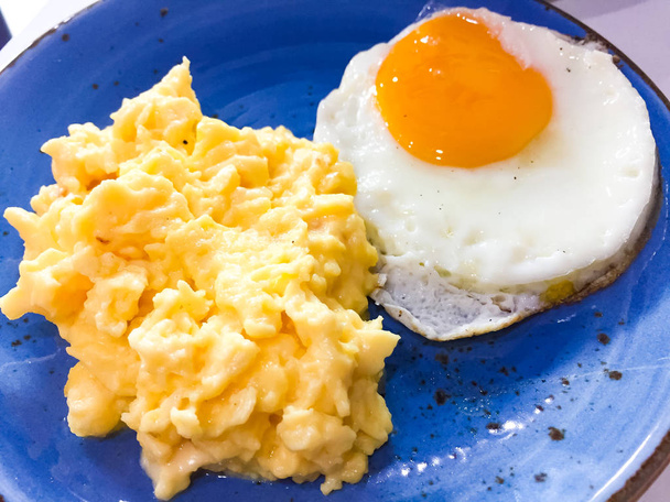 Frühstück, Rührei mit Käse und mittleres Spiegelei, das auf die blaue Schüssel gelegt wurde. Das ist Essen am Morgen - Foto, Bild