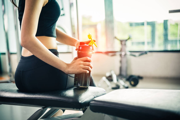 Asian beautiful woman drinking protein shake or drinking water in sport fitness training gym. Sports and people concept. Fitness and workout theme.  Sun flare effect - Zdjęcie, obraz