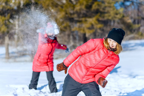 Outdoor portrait of two young girls in bright jackets, playing snowballs in a winter park. having fun throwing snow - Φωτογραφία, εικόνα