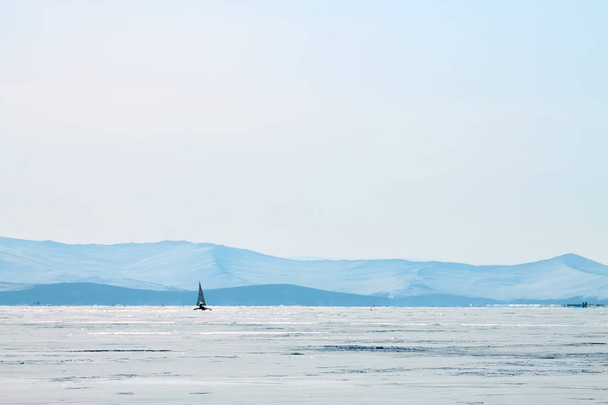 Ice boat rides on the ice of Lake Baikal in the background Olkhon in the winter foggy morning away - Photo, image