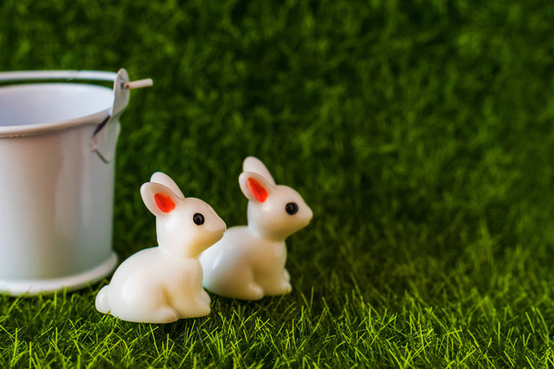 Dois coelhos em miniatura com um balde. figuras na grama close-up
 - Foto, Imagem