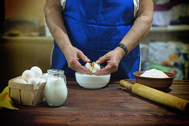 elderly woman adds eggs into dough for bread - Photo, image