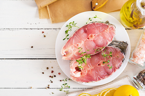 Raw steak of carp fish with lemon and thyme  on white wooden background. Preparing fish for roasting in parchment paper. Diet menu. Top view. Flat lay - Photo, Image