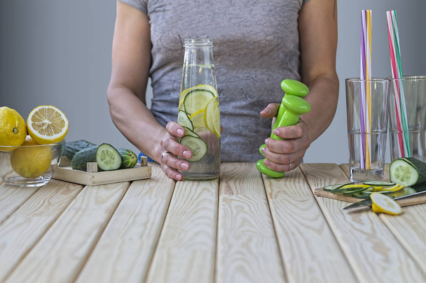 Жінка тримає пляшку детоксикаційного огірка, лимонів і гантелі для пристосування. Поняття: здоровий спосіб життя
 - Фото, зображення