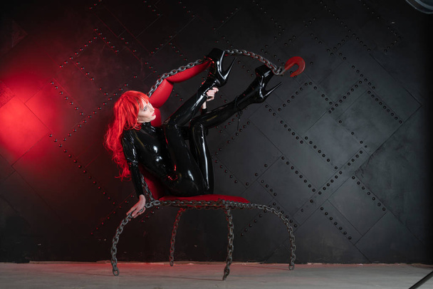 dangereux fétiche cruel fille aux cheveux roux posant en noir bdsm vêtements en latex à la chaise des chaînes dans le style de sadomasochisme
 - Photo, image