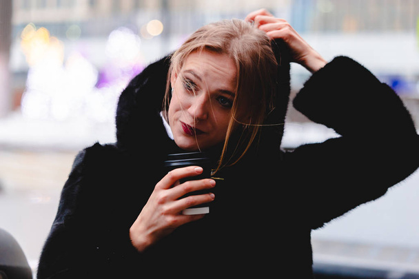 A girl in a black coat in cold weather in the business center of the city. - Valokuva, kuva