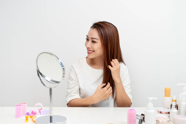 Belle jeune femme regardant reflet dans le miroir tout en brossant les cheveux longs à la coiffeuse
 - Photo, image