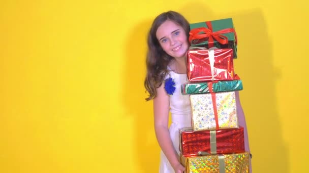 Šťastná dívka v bílých šatech usměje a skrývá mnoho dárkových krabiček v ruce na žlutém podkladu - Záběry, video