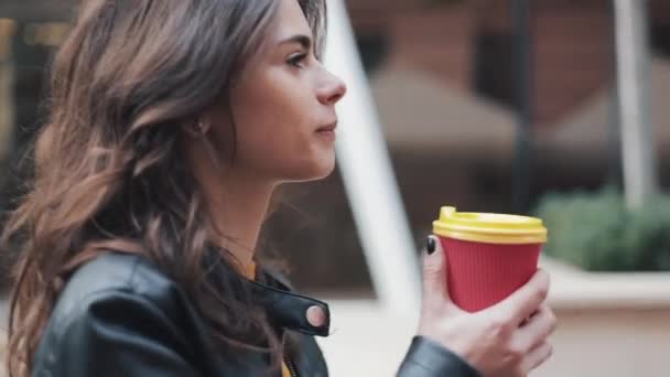 Beautiful young woman with an attractive appearance, adorable look and autumn jacket in the city. Amazing view of business lady with a cup of coffee walking down the city street - Filmagem, Vídeo