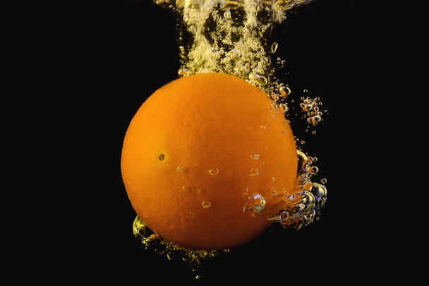 Яркий спелый апельсин падает в воду, когда он разрывает поверхность
 - Фото, изображение