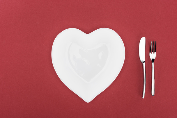 elevated view of heart shaped plate and cutlery isolated on red, st valentine day concept - Foto, imagen