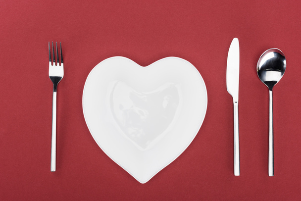 view from above of heart shaped plate and cutlery isolated on red, st valentine day concept - Valokuva, kuva