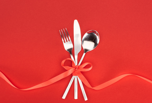 flat lay with fork, knife and spoon wrapped by red festive ribbon isolated on red, st valentine day concept - Photo, Image