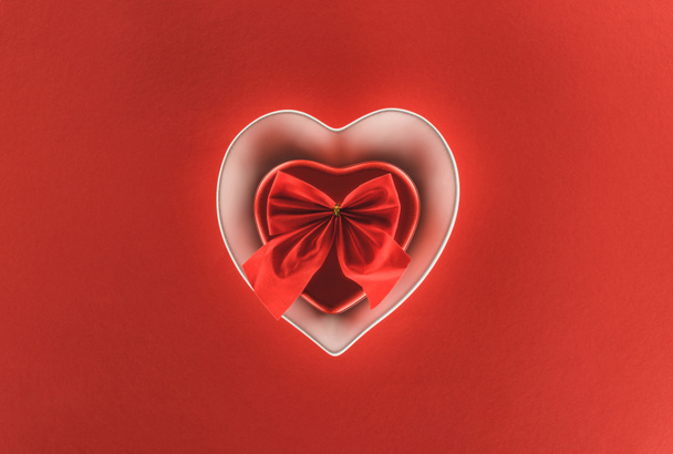top view of heart shaped present box and festive ribbon isolated on red, st valentine day concept - 写真・画像