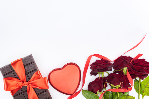 το Top view σοκολάτας τυλιγμένο με εορταστική κορδέλα, κόκκινα τριαντάφυλλα και απομονωθεί σε λευκό, Αγίου Βαλεντίνου ημέρα ιδέα δώρο κουτί σε σχήμα καρδιάς - Φωτογραφία, εικόνα