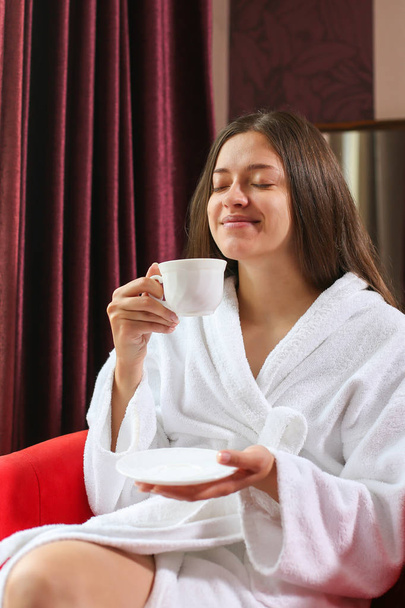 Portrait of the beautiful woman dressed in a bathrobe drinking tea in the morning in the hotel room.  - Zdjęcie, obraz