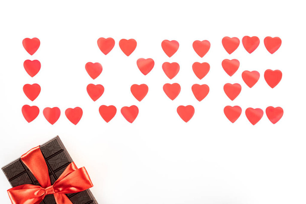 plochý ležela s nápisy love vyrobená z symbolů srdce a čokoládou zabalené slavnostní stuhou izolované na bílém, st valentine den koncept - Fotografie, Obrázek