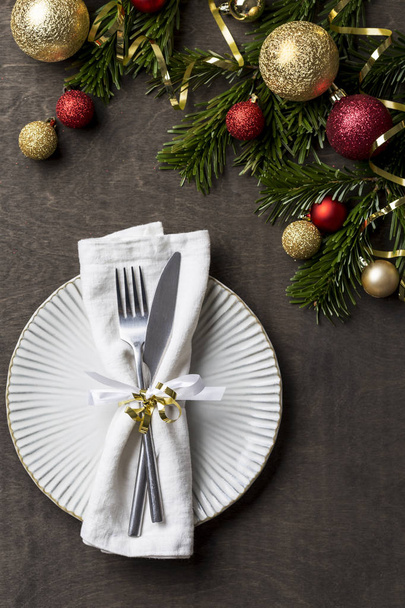 Christmas dinner table with white plate, fork, knife and napkin, Christmas festive decor around. Traditional Christmas decorations. Romantic table setting - Foto, Imagen