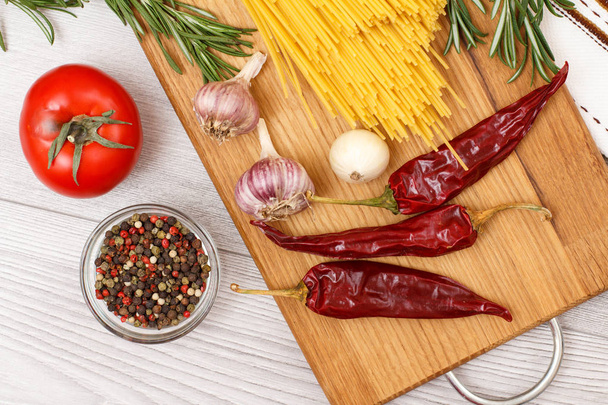 Těstoviny nebo špagety s ingredience pro vaření maso nebo ryby na dřevěném prkénku. Česnek, nové koření paprika v skleněná mísa, chilli, rajčaty, cibulí a rozmarýnem. Pohled shora. - Fotografie, Obrázek