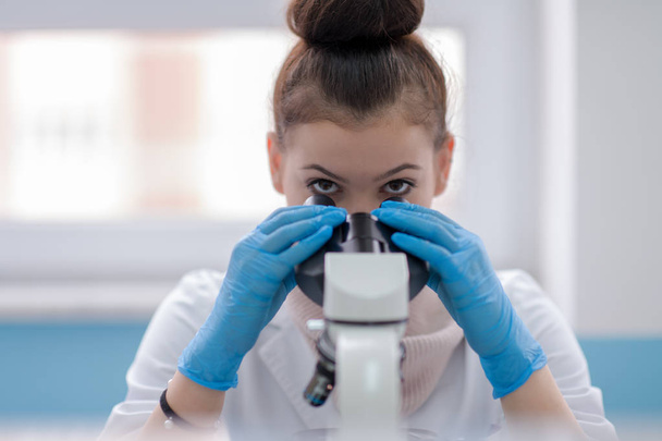 Young female student scientist looking through a microscope while doing some research in the laboratory - Photo, Image