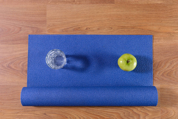 Blue yoga mat and glass of water and apple - Photo, image