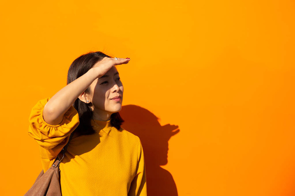 Азіатський жінка всміхається на помаранчевий Топ з руки на чолі, дивлячись на камеру в помаранчевому фоні - Фото, зображення