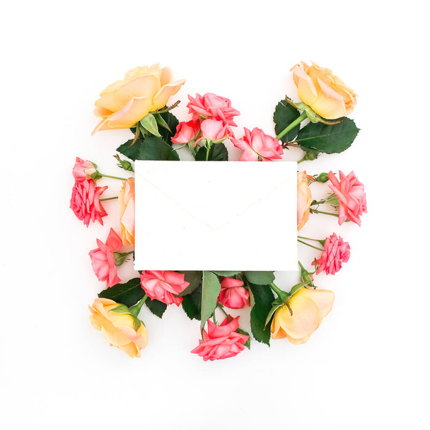 Paper envelope with red and orange roses and leaves on white background. Flat lay, top view. Beauty concept - Photo, Image