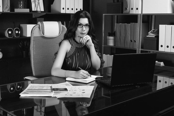 Retrato de jovem mulher de negócios bonita em terno de moda e óculos trabalhando na mesa de computador preto elegante
 - Foto, Imagem